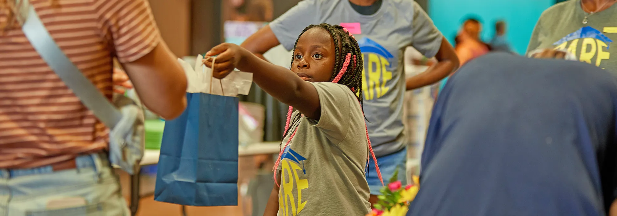 718A9318 A young CARE volunteer hands a woman a bag of health care items during a community event.